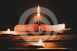 Open Holy Bible and candle on a old oak wooden table.