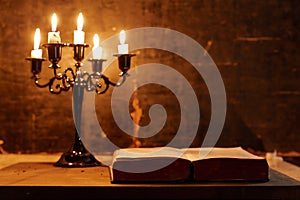 Open Holy Bible and candle on a old oak wooden table.