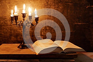 Open Holy Bible and candle on a old oak wooden table.