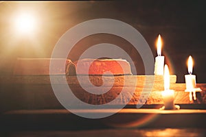 Open Holy Bible and candle on a old oak wooden table. Beautiful gold background.