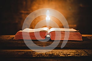 Open Holy Bible and candle on a old oak wooden table. Beautiful gold background.