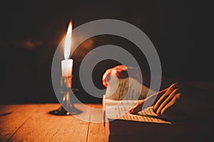 Open Holy Bible and candle on a old oak wooden table. Beautiful gold background.