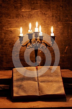 Open Holy Bible and candle on a old oak wooden table. Beautiful gold background.