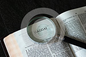 Open Holy Bible Haggai the prophet from Old Testament with a magnifying glass on dark granite background