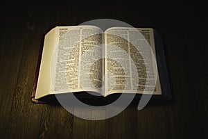 Open Holy Bible over a wooden table at night