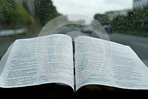 Open Holy Bible in Psalm 121 in rainy day. Blurred background with expressway and cars.