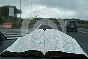 Open Holy Bible in Psalm 91. Windshield with raindrops. Blurred background with expressway.