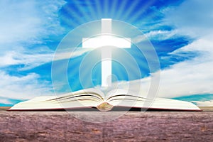 Open holy bible with white cross in the blue sky back ground.