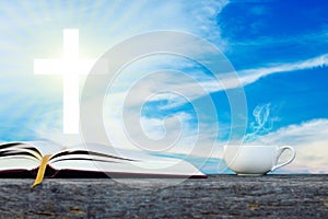 Open holy bible with white cross in the blue sky back ground.