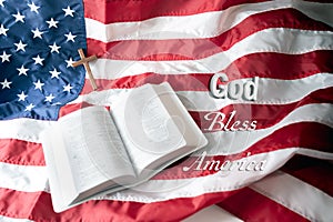 Open Holy bible and Wooden cross over American flag background. God bless America.selective focus