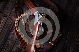 An open hunting rifle with cartridges and a knife in a leather case, lying on the wooden background