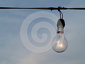 Open incandescent light bulb hang on old electric wire with gloomy dusk sky