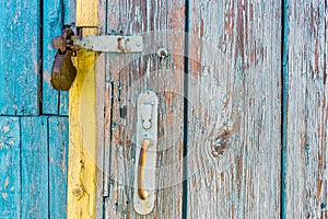 Open iron padlock on a battered wooden door with weathered cracks of blue and yellow colors of old country house