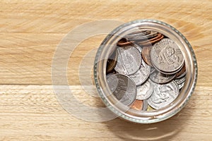 An open jar with small coins of American cents stands on a wooden table, close-up, selective focus. A concept for business and fin