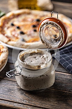 An open jar with a yeast starter and a sourdough pizza in the background