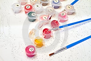 Open jars of watercolor paint and brushes for painting by numbers on the background of a canvas with numbers