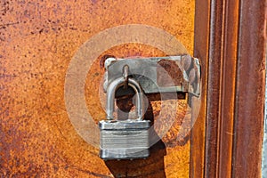 Open key lock hanging on closed orange rusty metal door - not very secure