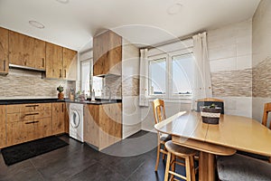 An open kitchen with chestnut wood furniture, black synthetic stone countertops, several windows, large stone floors