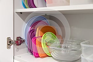 Open kitchen cupboard full of plastic and glass containers inside.