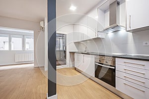 Open kitchen in empty room with gray metal pillar and newly installed white kitchen cabinet with integrated stainless steel