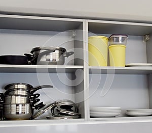 Open kitchen furniture with utensils inside such as pans, saucepans, plates and bowls