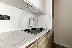 Open kitchen of a loft-type home with oak wood furniture, black resin sink with faucet of the same color and white painted walls