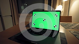 Open laptop with chromakey screen on kitchen table at night