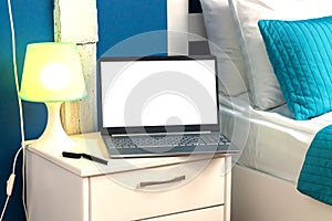 Open laptop computer with blank monitor next to lamp on bedside table