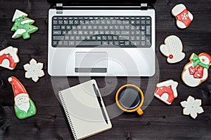 Open laptop computer, blank notebook, cup of coffee and Christmas gingerbread cookies on dark wood background, copy space.