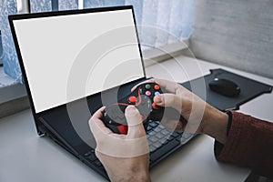 Open laptop computer with a blank white screen with copy space standing open on table alongside a video game controller indoors at