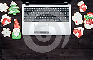Open laptop computer and Christmas gingerbread cookies on dark wood background, copy space. Top view, flat lay. Santa, snowflake.