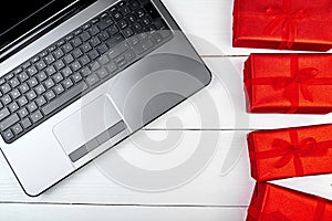 Open laptop computer and red gift boxes on white wooden desk in office, copy space. Flat lay, top view. Online shopping,  holiday