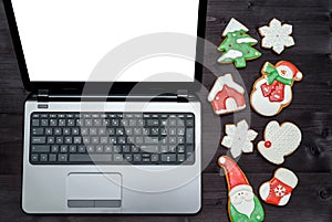 Open laptop computer with white blank screen and Christmas gingerbread cookies on dark wooden background, copy space.