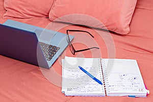 Open laptop, diary and glasses on a bed in a bedroom. I work from home, comfortable form of communication or entertainment.