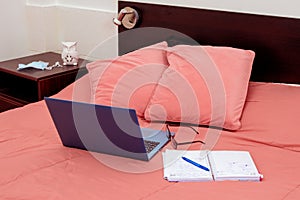 Open laptop, diary and glasses on a bed in a bedroom. I work from home, comfortable form of communication or entertainment.