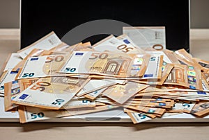 Open laptop and pile of money euro banknotes