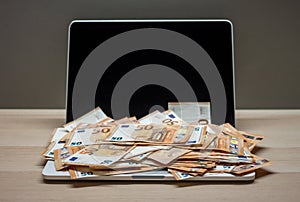 Open laptop and pile of money euro banknotes