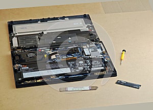 An open laptop on a workbench with its back cover removed, internal components m.2 NVME SSD upgrade in progress, tools pry spudger