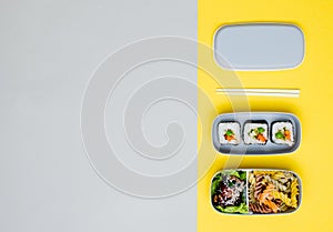 Open lunch box filled with vegan rolls, vegetable pasta and chicken on yellow and grey background