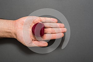 Open male palm with a red heart-shaped jewelry box. Present. Black background