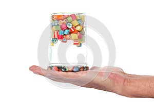 Open man`s hand and a glass jar half full of colored candies turned up side down isolated on white background with  clipping path