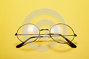 Open metal rimmed spectacles isolated on yellow, top view.