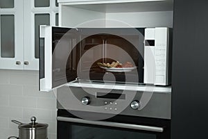 Open microwave oven with food on white shelf in kitchen
