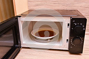 Open microwave with soup inside. Image of the microwave oven. Modern microwave oven at home