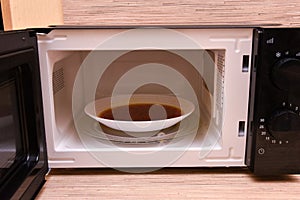 Open microwave with soup inside. Image of the microwave oven. Modern microwave oven at home