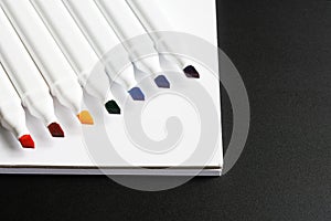 Open multi-colored felt-tip markers and a white notepad on a dark background. Rainbow color sequence. Concept of teaching