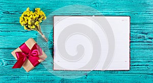 Open notebook with blank pages, gift box with ribbon and flowers.