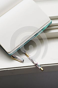 Open notebook with blank pages and a pen on a windowsill