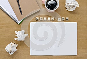 Open notebook and coffee cup on a writers desk, with tiles spelling out `Write now`