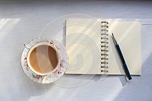 Open notebook and cup of tea on a sunny table top.